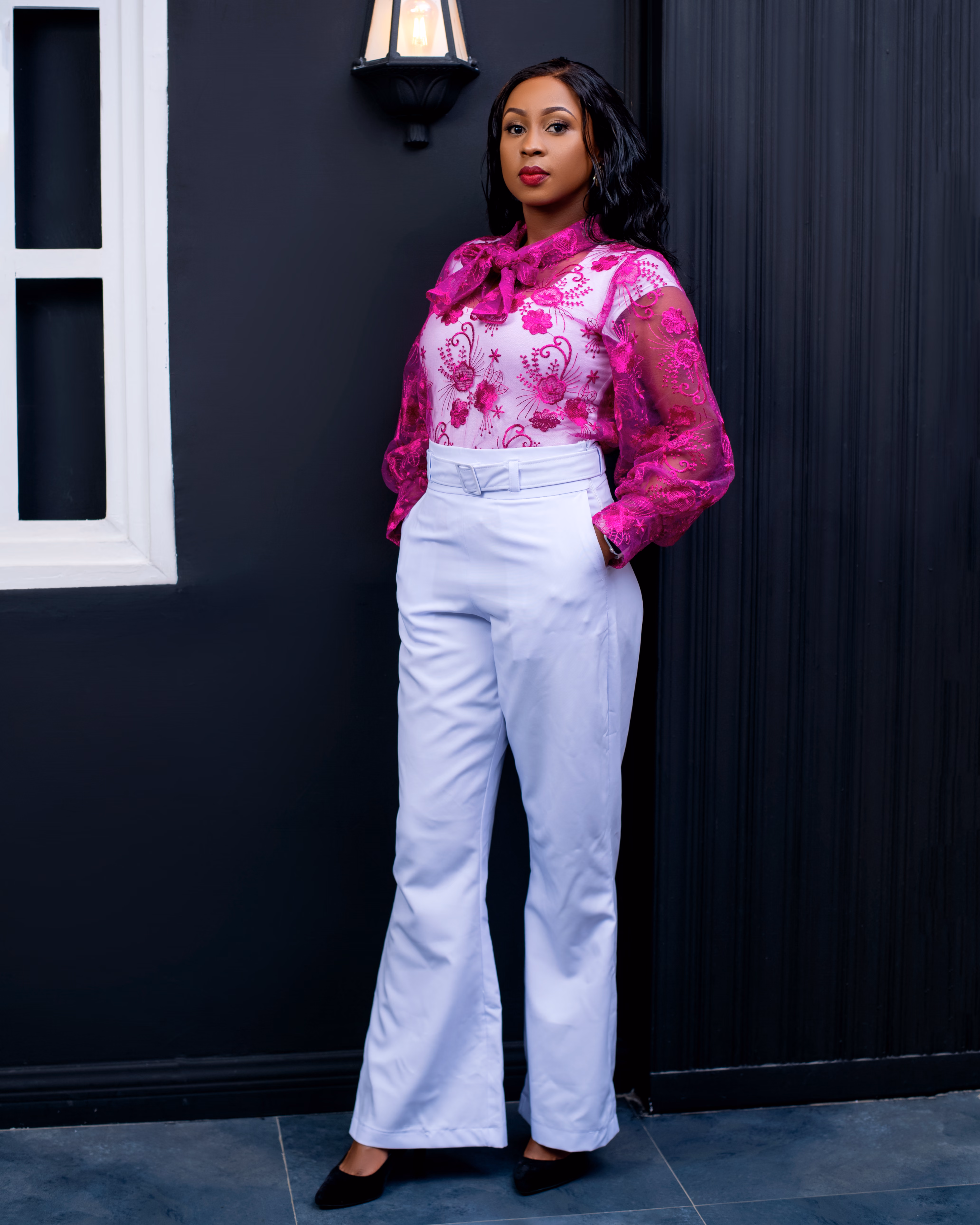 Joy Mido standing in a pink blouse and white trousers